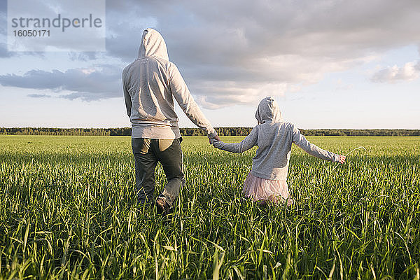Vater und Tochter halten sich an den Händen  während sie inmitten von Pflanzen in einer Landschaft spazieren gehen