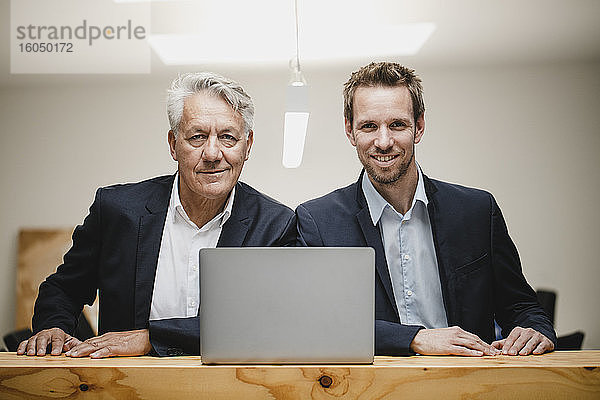 Zwei selbstbewusste Geschäftsleute sitzen im Büro  benutzen einen Laptop und lächeln