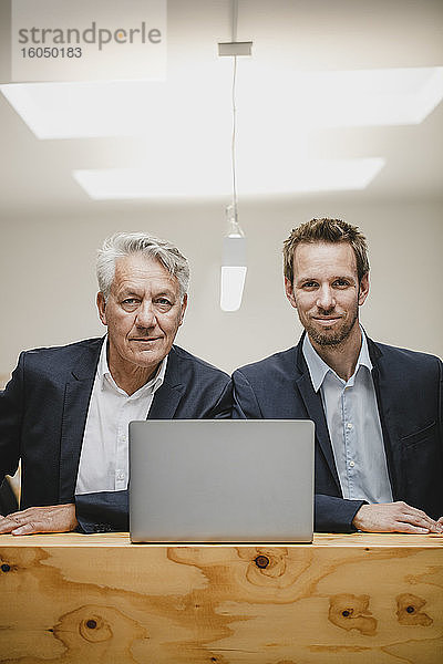 Zwei selbstbewusste Geschäftsleute sitzen im Büro  benutzen einen Laptop und lächeln