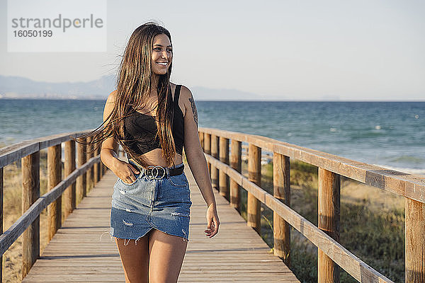 Schönes Teenager-Mädchen zu Fuß auf der Promenade am Strand gegen klaren Himmel