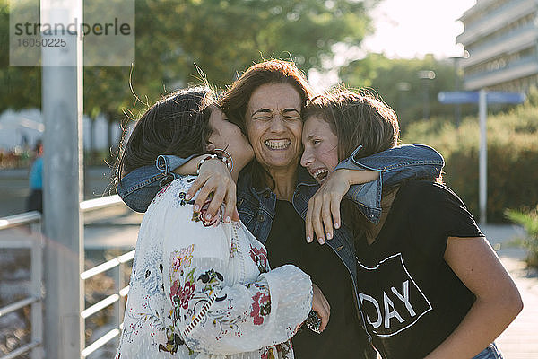 Fröhliche  liebende Mutter  die ihre Töchter umarmt  während sie im Freien steht