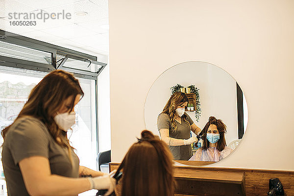 Friseurin mit Maske und Glättmaschine