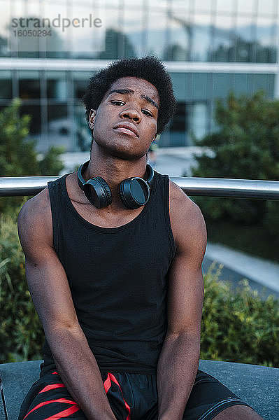 Porträt eines selbstbewussten jungen Mannes mit Kopfhörern  der in der Stadt sitzt