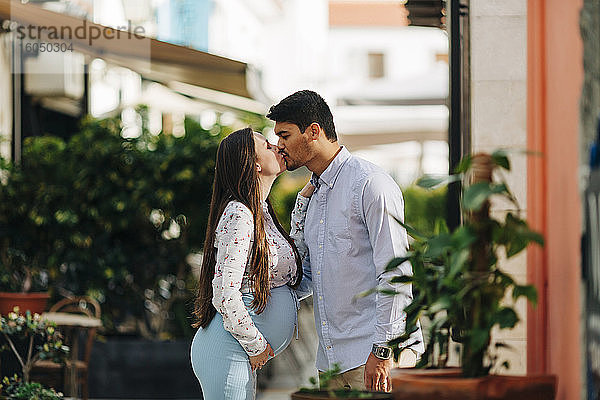 Romantisches schwangeres Paar küsst sich in der Stadt an einem sonnigen Tag