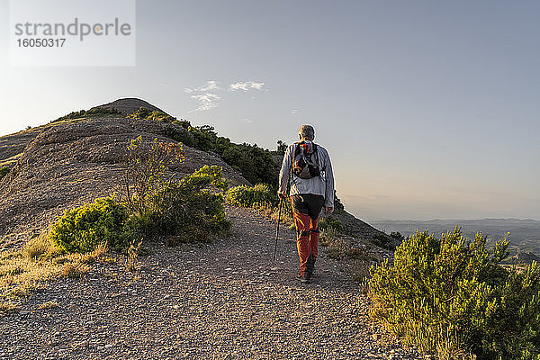 Aktiver älterer Mann mit Wanderstock auf einem Berg bei Sonnenuntergang