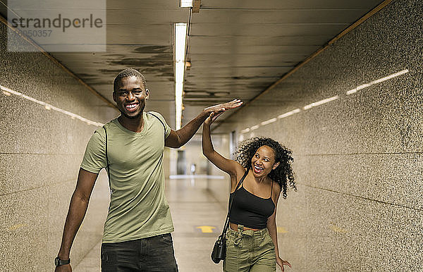 Fröhliches Paar gibt sich beim Gehen im unterirdischen Gang einer U-Bahn-Station die Hand