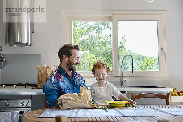 Glücklicher Vater und Sohn  die am Esstisch mit grünen Erbsen in der Küche sitzen und genießen