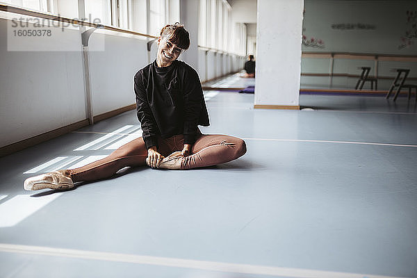 Glückliche Balletttänzerin streckt die Beine auf dem Boden im Studio