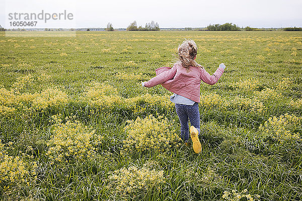 Mädchen in gelben Gummistiefeln läuft in der Nähe eines Rapsfeldes
