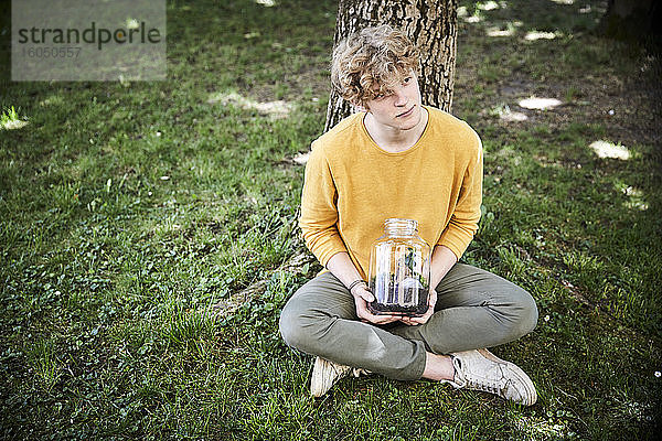 Porträt eines jungen Mannes im Garten sitzend mit Pflanzen in einem Glas