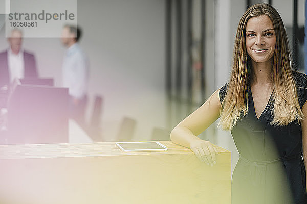 Geschäftsfrau in einem Büro stehend  auf einen Holztresen gestützt  lächelnd