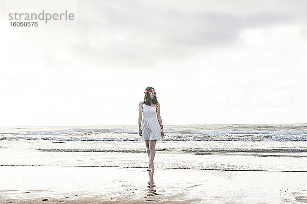 Junge Frau in weißem Kleid geht am Ufer gegen das Meer