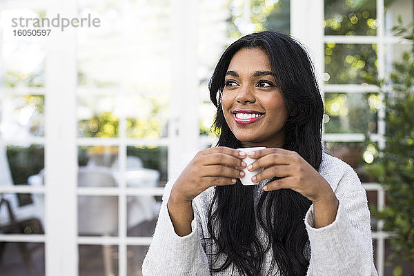 Nachdenkliche junge Frau lächelt  während sie eine Kaffeetasse im Café hält