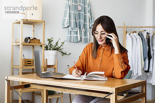 Weibliche Modedesignerin  die zu Hause am Schreibtisch sitzt und Notizen macht