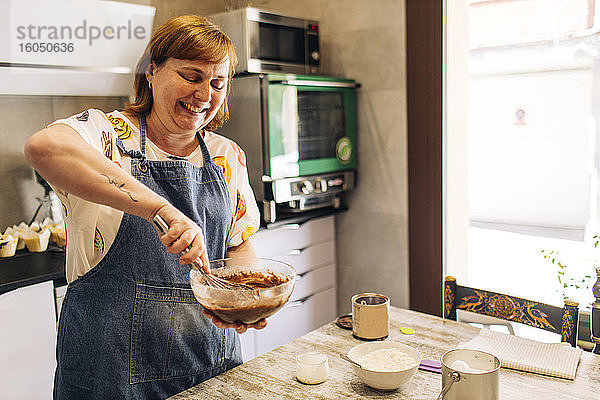 Lächelnde Bäckerin mischt Kuchenteig in einer Schüssel auf einem Tisch in einer Werkstatt
