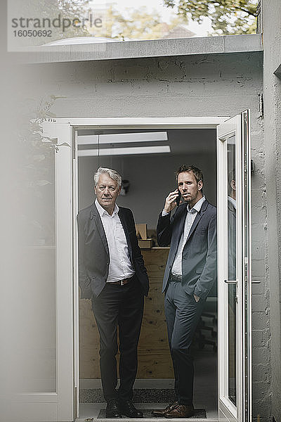 Zwei Geschäftsleute  die in einer offenen Bürotür stehen und telefonieren