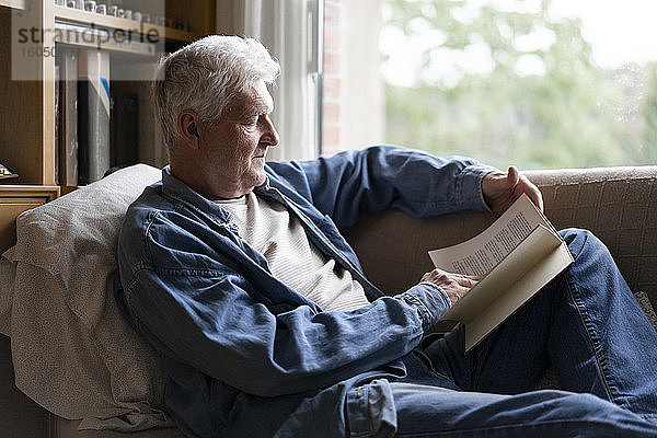 Älterer Mann liest ein Buch und entspannt sich auf dem Sofa zu Hause