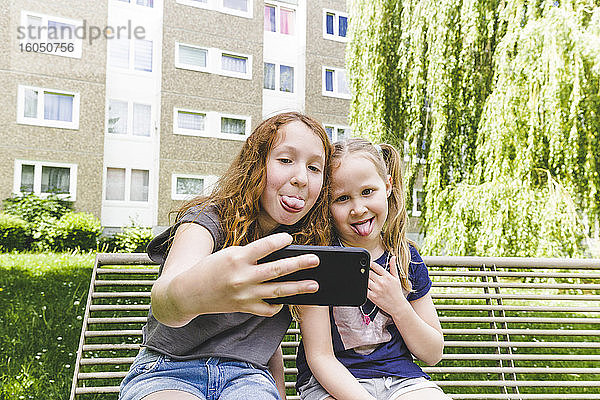 Schwestern machen Selfie mit herausgestreckten Zungen im Park