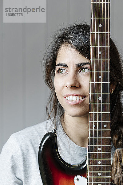 Nachdenkliche junge Frau mit E-Gitarre an der Wand zu Hause