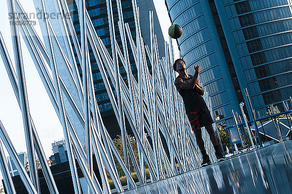 Junger Mann spielt Basketball in moderner Stadtumgebung
