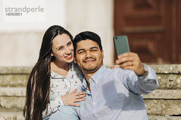 Glückliches schwangeres Paar  das ein Selfie mit seinem Smartphone an einem sonnigen Tag macht