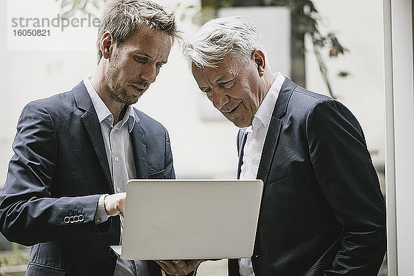 Zwei Geschäftsleute stehen im Büro und benutzen einen Laptop