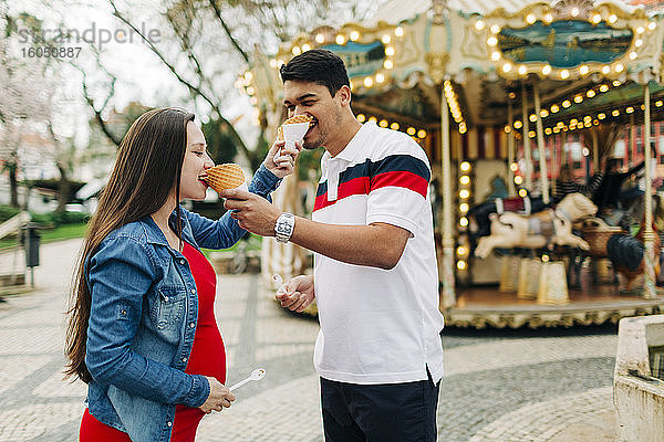 Glückliches schwangeres Paar  das sich vor einem Vergnügungspark mit Eiscreme füttert  Cascais  Portugal