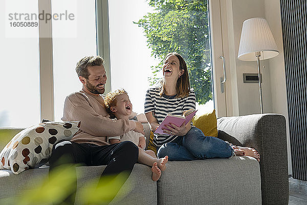 Fröhliche Familie  die zu Hause auf dem Sofa sitzend ein Märchenbuch liest