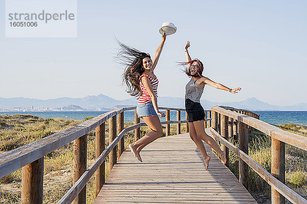 Aufgeregte Teenager-Mädchen springen auf der Promenade am Strand gegen den klaren Himmel