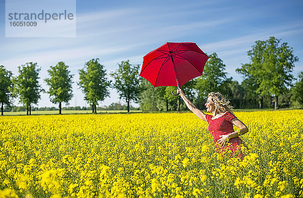 Glückliche Frau mit rotem Regenschirm inmitten von Ölsaatenrapsen