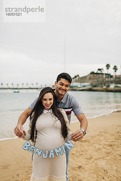Glückliches schwangeres Paar mit Namensschild am Strand  Cascais  Portugal