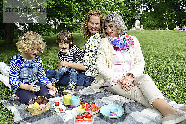 Glückliche Kinder genießen ihr Picknick mit Mutter und Großmutter im öffentlichen Park