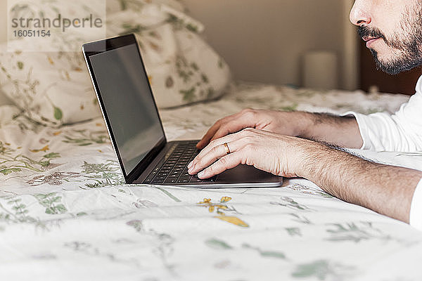 Mann mit Laptop auf dem Bett