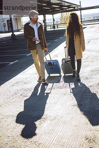 Business-Paar zieht Gepäck auf dem Flughafenparkplatz an einem sonnigen Tag