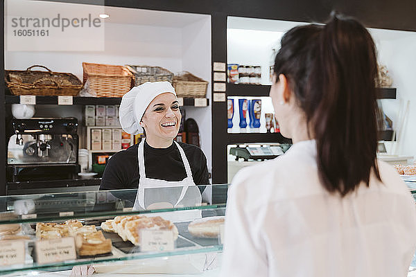 Glückliche Bäckerin  die einen Kunden in einer Bäckerei bedient