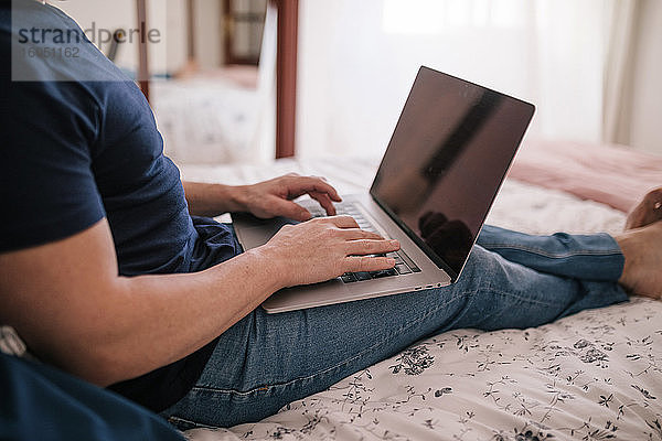 Reifer Mann benutzt Laptop  während er zu Hause auf dem Bett sitzt