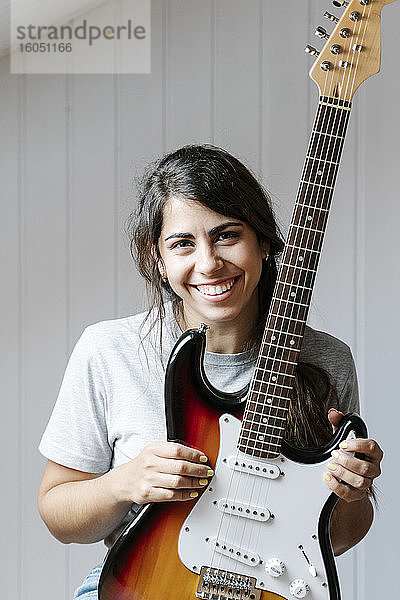 Glückliche Frau hält E-Gitarre gegen die Wand zu Hause