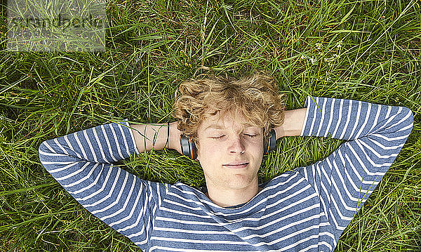 Porträt eines jungen Mannes mit lockigem blondem Haar  der auf einer Wiese liegt und mit Kopfhörern Musik hört