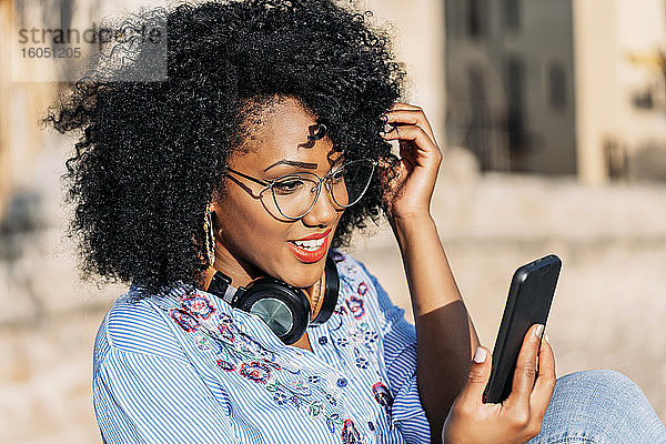 Lächelnde Frau mit Afro-Haar und Brille während eines Videoanrufs im Freien