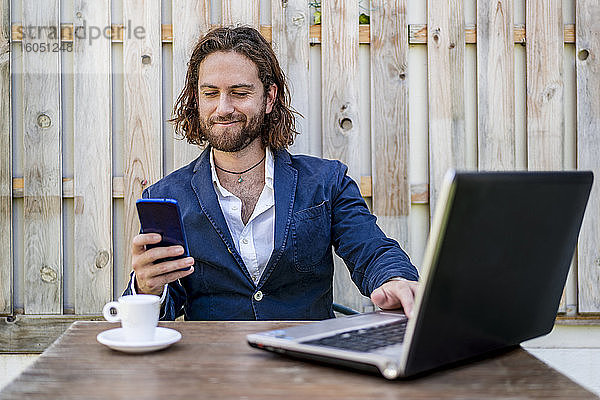 Geschäftsmann  der grinsend ein Mobiltelefon benutzt  während er in einem Café sitzt