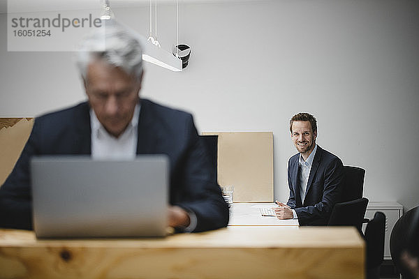 Geschäftsmann lächelnd im Büro mit älteren Kollegen arbeiten im Vordergrund