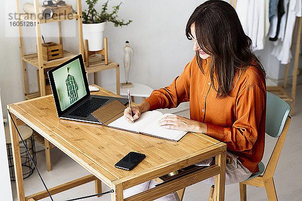 Weibliche Modedesignerin  die zu Hause am Schreibtisch sitzt und Notizen macht