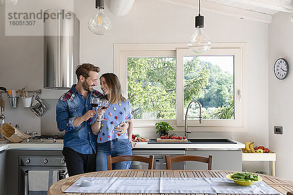 Glückliches Paar in der Mitte des Erwachsenenalters genießt Wein  während es in der Küche zu Hause steht