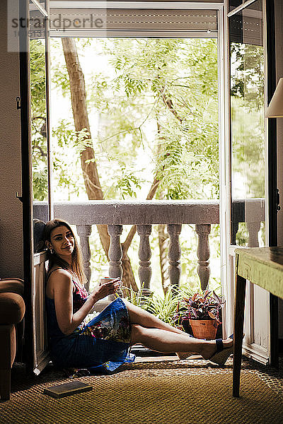 Frau genießt Kaffee  während sie auf dem Balkon zu Hause sitzt