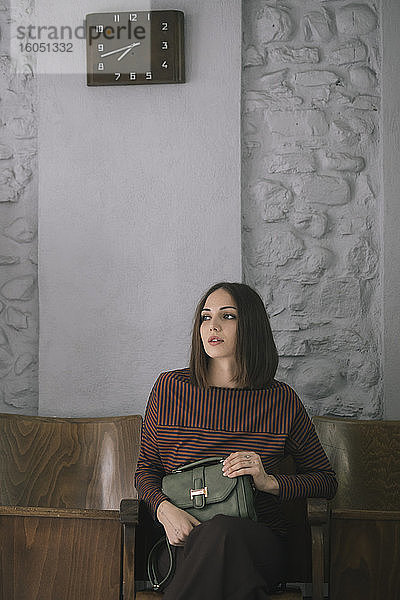Nachdenkliche junge Frau mit Handtasche auf einem Stuhl im Designstudio sitzend