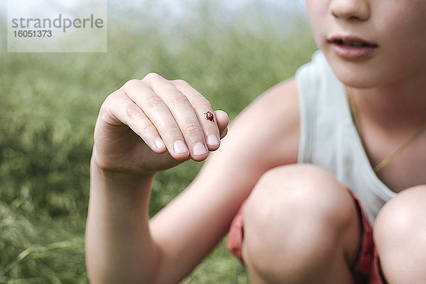 Ausschnittansicht eines Jungen in der Natur mit Marienkäfer am Finger