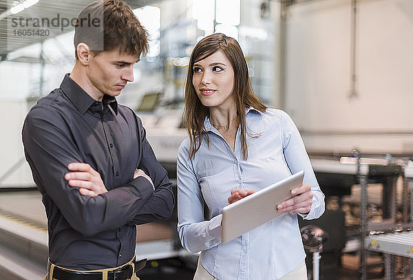 Geschäftsfrau zeigt einem männlichen Kollegen ein digitales Tablet  während sie in einer Fabrik steht