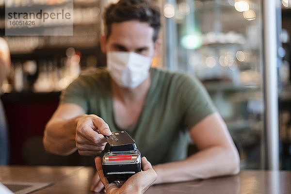 Mann mit Schutzmaske bezahlt mit Kreditkarte in einem Restaurant
