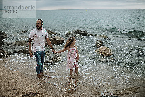 Vater und Tochter halten sich am Strand an den Händen
