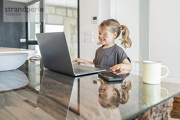 Lächelndes süßes Mädchen studiert über Laptop auf Tisch zu Hause